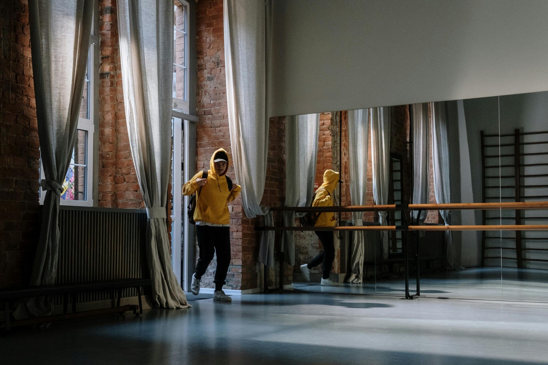 A dancer in a yellow hoodie enters a bright, spacious dance studio, reflecting vibrant energy and passion for Salsa and Bachata.
