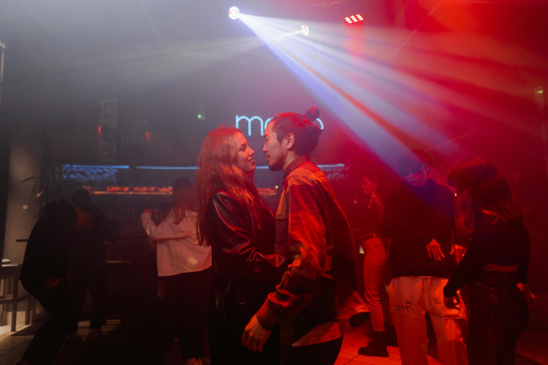 Couples dancing closely in a vibrant salsa and bachata dance studio filled with colorful lights and a lively atmosphere.