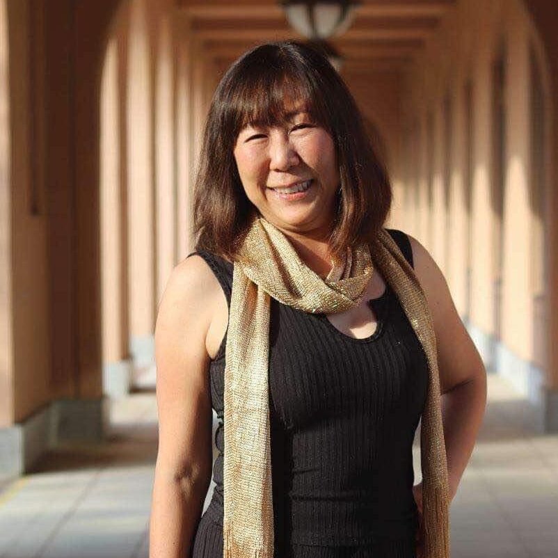 Photo of Yoko, Dream Team Member, wearing a black dress and a gold scarf