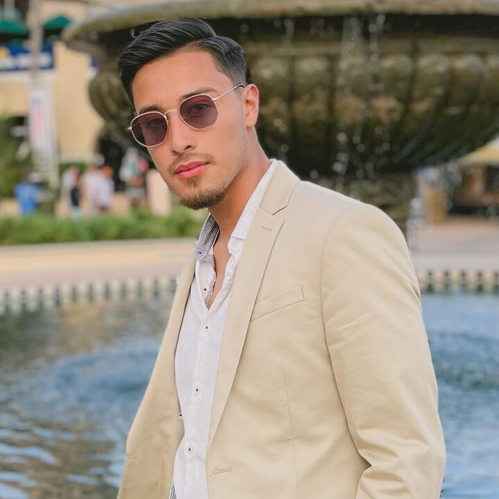 Stylish young man in beige suit poses confidently near a fountain, promoting a vibrant Salsa and Bachata dance studio.